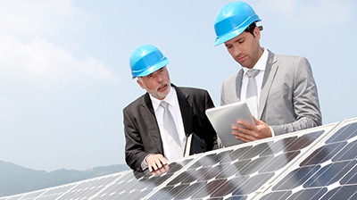 Two businessmen standing over solar panels reviewing items on a tablet